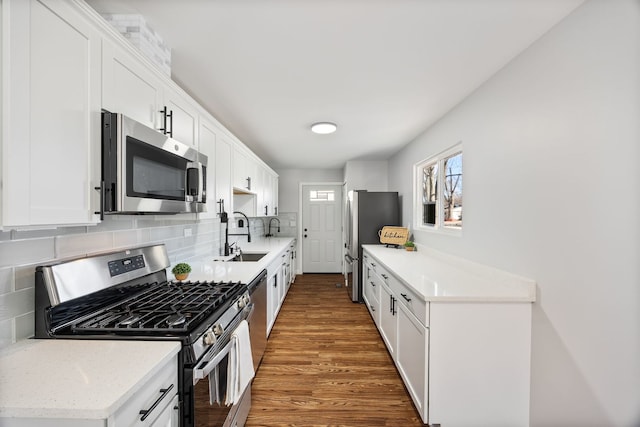 kitchen with wood finished floors, a sink, decorative backsplash, appliances with stainless steel finishes, and white cabinetry