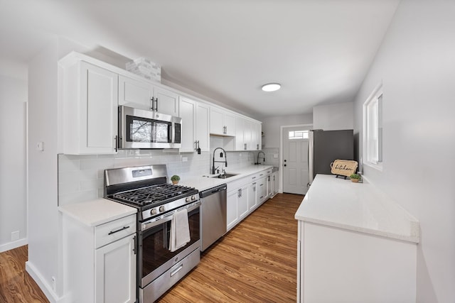 kitchen with a sink, white cabinets, appliances with stainless steel finishes, light wood-type flooring, and backsplash