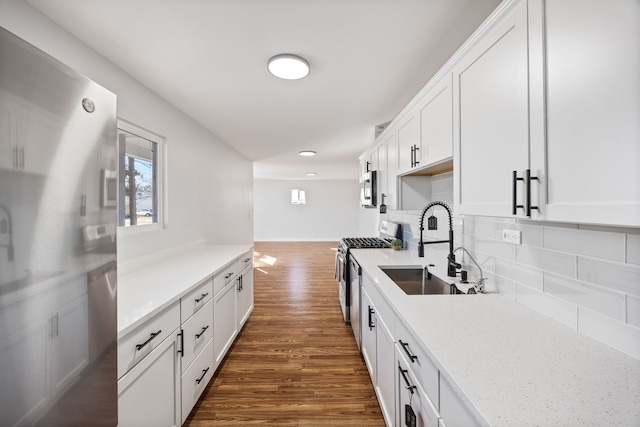 kitchen with a sink, backsplash, dark wood finished floors, stainless steel appliances, and white cabinets