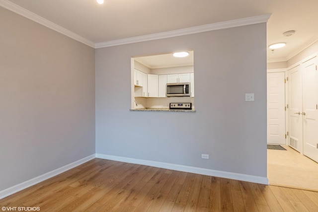 empty room featuring baseboards, crown molding, and light wood finished floors