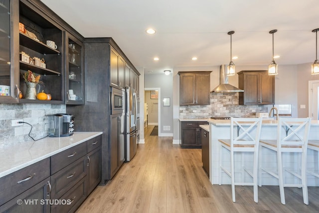 kitchen featuring light wood finished floors, backsplash, wall chimney range hood, decorative light fixtures, and a kitchen bar