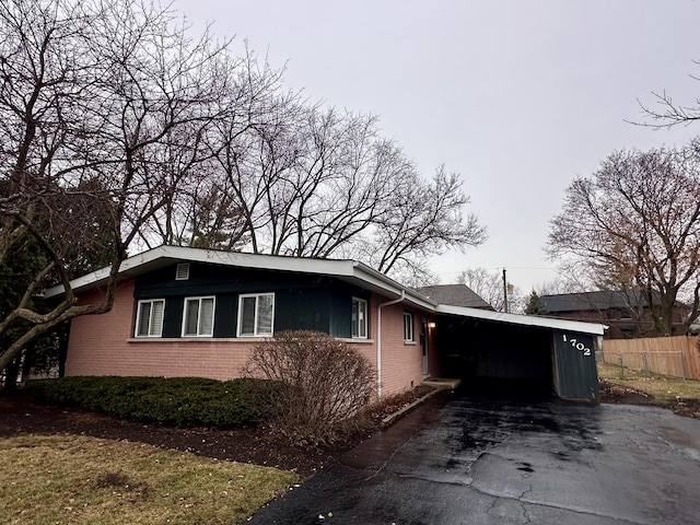 view of side of home featuring a carport, brick siding, driveway, and fence