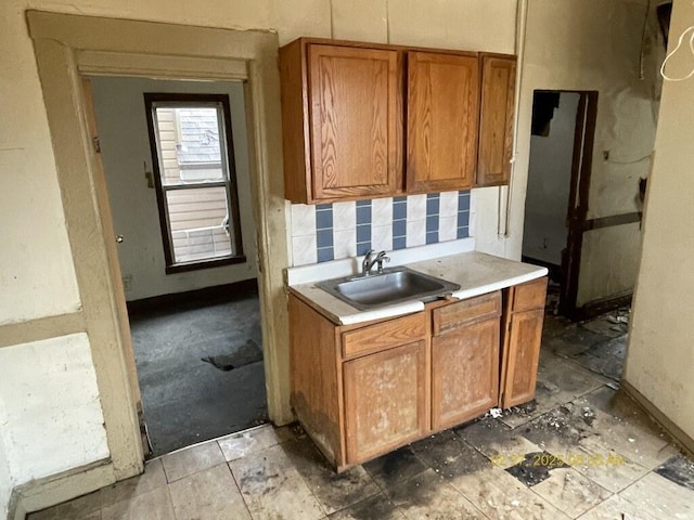 kitchen featuring baseboards, a sink, light countertops, brown cabinets, and backsplash