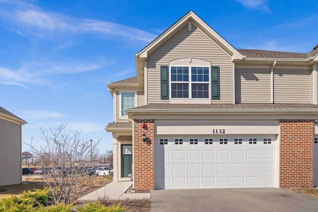 traditional-style home with aphalt driveway, a garage, a shingled roof, and brick siding