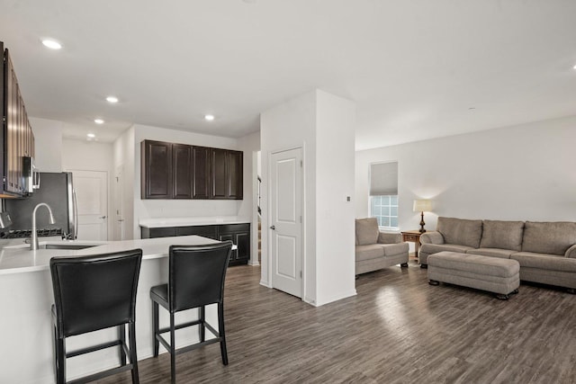 kitchen featuring dark brown cabinets, dark wood-type flooring, open floor plan, a breakfast bar, and a sink