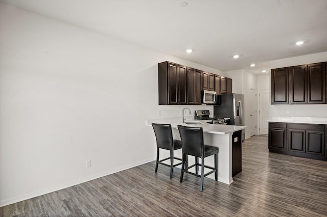 kitchen featuring a breakfast bar, dark wood finished floors, a sink, light countertops, and appliances with stainless steel finishes
