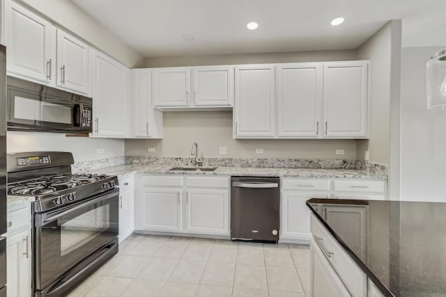 kitchen featuring light tile patterned flooring, white cabinets, stone countertops, black appliances, and a sink