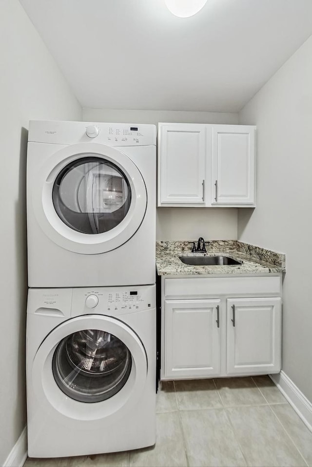 clothes washing area featuring light tile patterned floors, baseboards, cabinet space, a sink, and stacked washer and clothes dryer