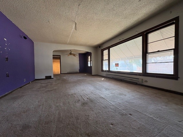 unfurnished room featuring a baseboard heating unit, ceiling fan, carpet floors, arched walkways, and a textured ceiling