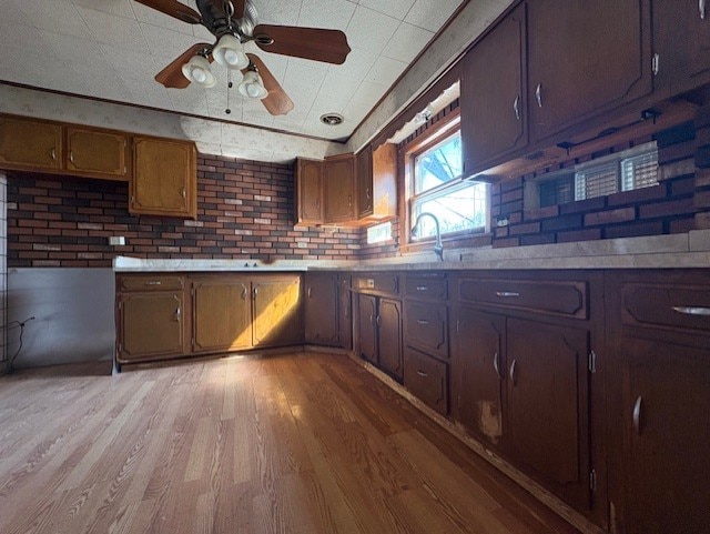 kitchen with a ceiling fan, a sink, light wood-style floors, brick wall, and light countertops