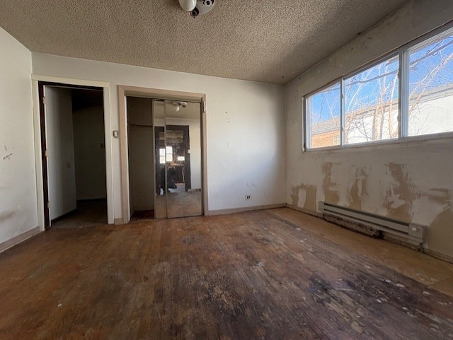 unfurnished bedroom with a baseboard heating unit, wood finished floors, two closets, and a textured ceiling