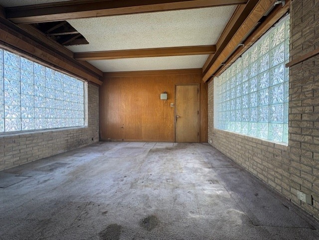 empty room with beam ceiling, a healthy amount of sunlight, and brick wall