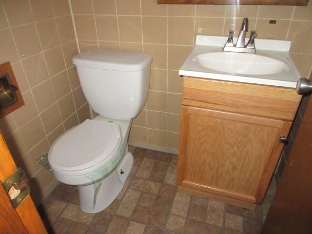 half bathroom featuring toilet, vanity, and tile walls