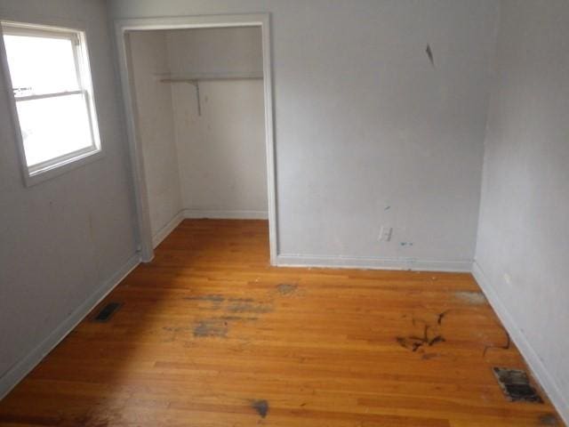 unfurnished bedroom featuring wood finished floors, visible vents, a closet, and baseboards