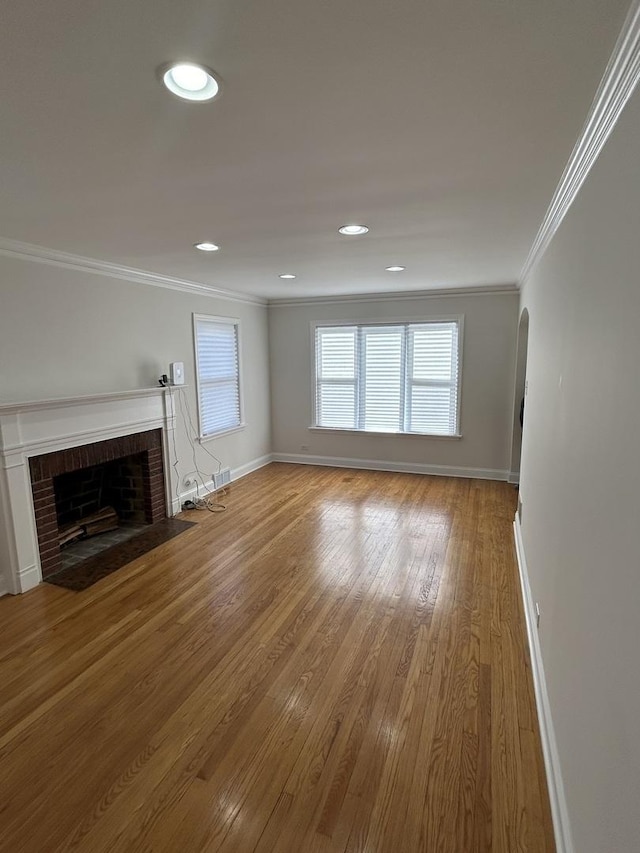 unfurnished living room with wood finished floors, a brick fireplace, baseboards, ornamental molding, and recessed lighting