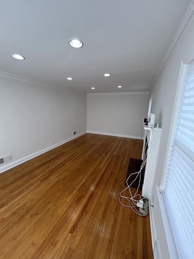 spare room with wood finished floors, crown molding, baseboards, and visible vents