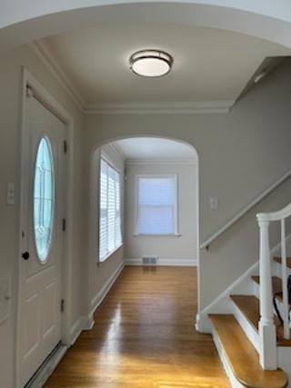 entrance foyer with crown molding, baseboards, stairs, arched walkways, and light wood-type flooring