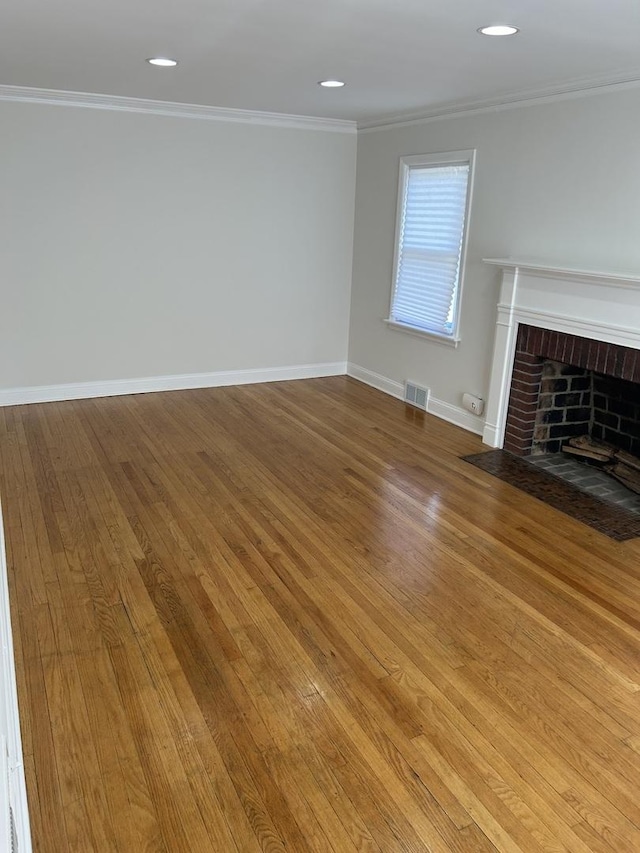 unfurnished living room with baseboards, visible vents, wood-type flooring, crown molding, and a brick fireplace