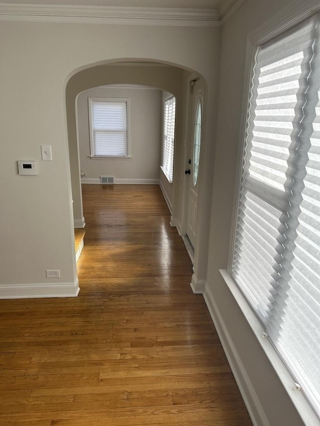 hall featuring baseboards, arched walkways, wood finished floors, and crown molding