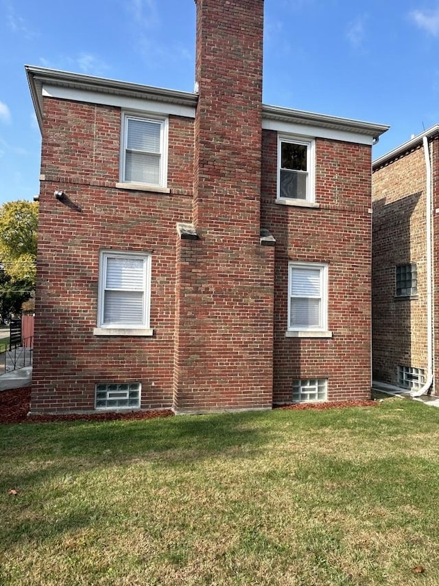 view of side of home with brick siding, a chimney, and a yard