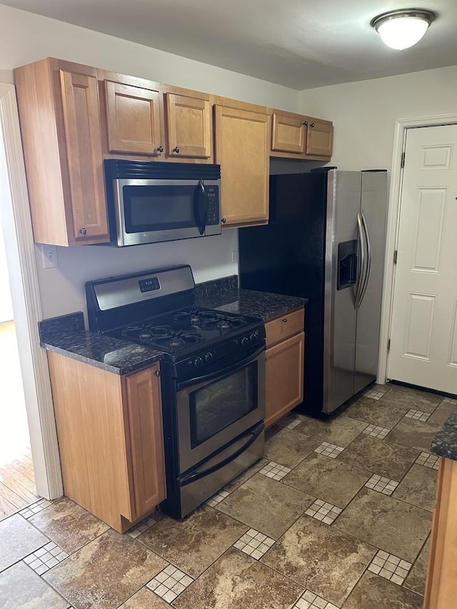 kitchen featuring dark stone counters, stone finish flooring, and stainless steel appliances