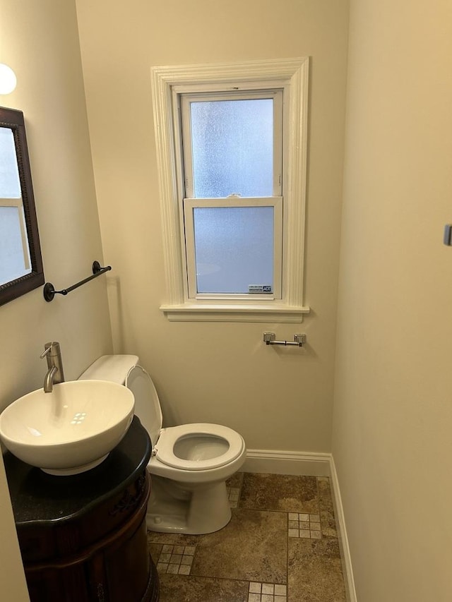 bathroom featuring toilet, stone finish flooring, baseboards, and a sink