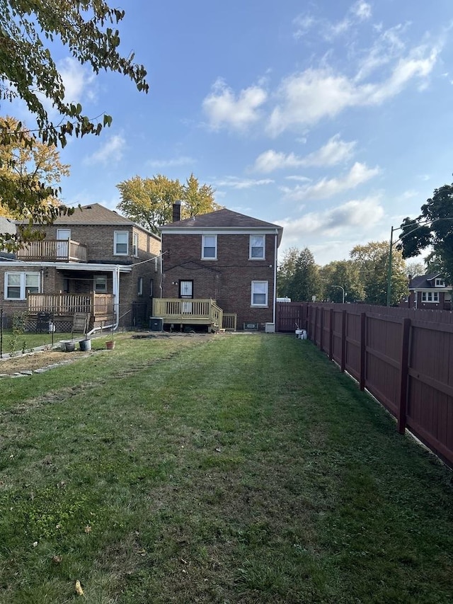 back of property with a fenced backyard, a deck, and a yard