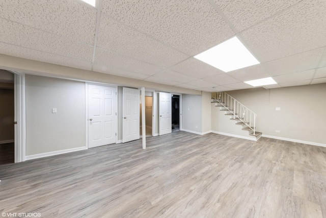 finished basement with a paneled ceiling, baseboards, wood finished floors, and stairs