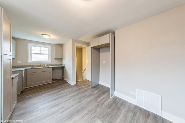 kitchen featuring visible vents, gray cabinets, a sink, light wood finished floors, and baseboards