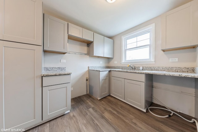 kitchen with a sink, light wood-type flooring, and light stone countertops