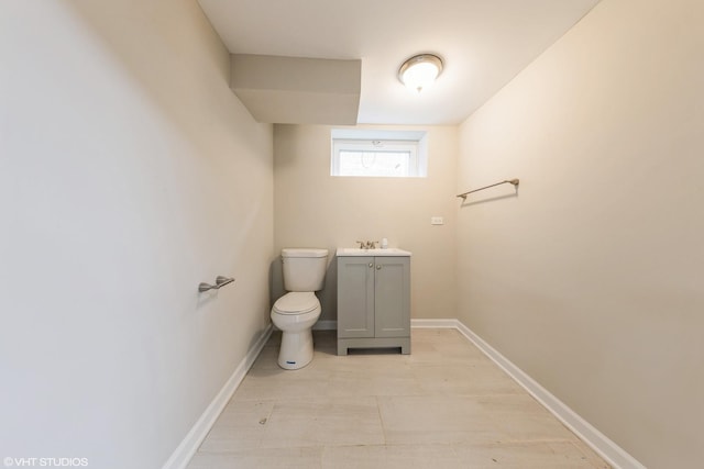 half bathroom with baseboards, toilet, and vanity