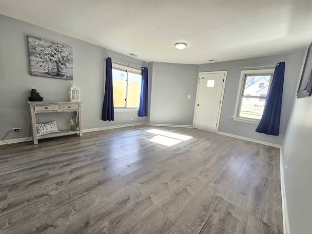 unfurnished living room with baseboards, plenty of natural light, visible vents, and wood finished floors