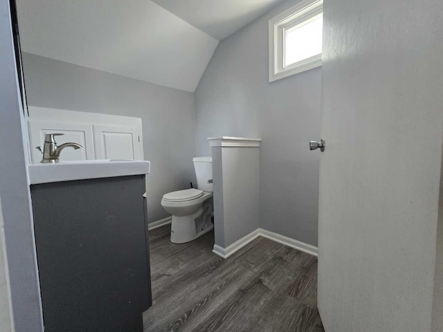 half bathroom with toilet, lofted ceiling, wood finished floors, baseboards, and vanity