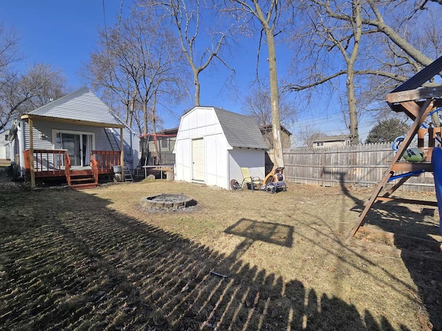 view of yard with an outbuilding, a wooden deck, a fenced backyard, a storage unit, and a fire pit