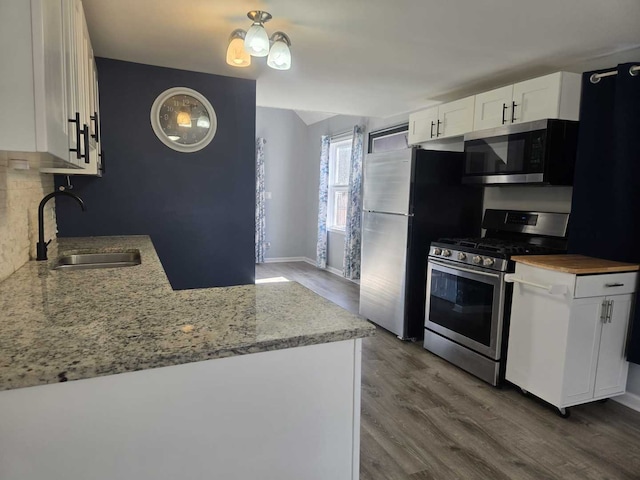 kitchen featuring a sink, light stone counters, wood finished floors, appliances with stainless steel finishes, and white cabinets