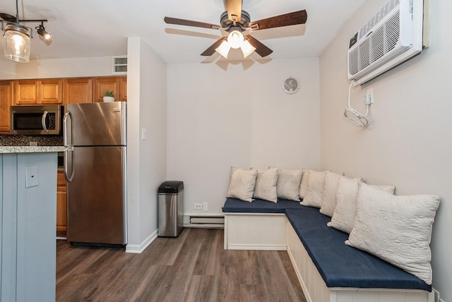 kitchen with an AC wall unit, dark wood finished floors, appliances with stainless steel finishes, baseboard heating, and ceiling fan