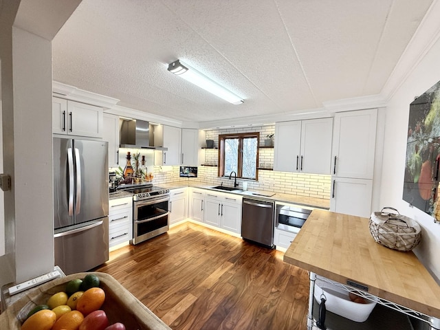 kitchen featuring a sink, stainless steel appliances, dark wood-type flooring, wall chimney range hood, and butcher block counters