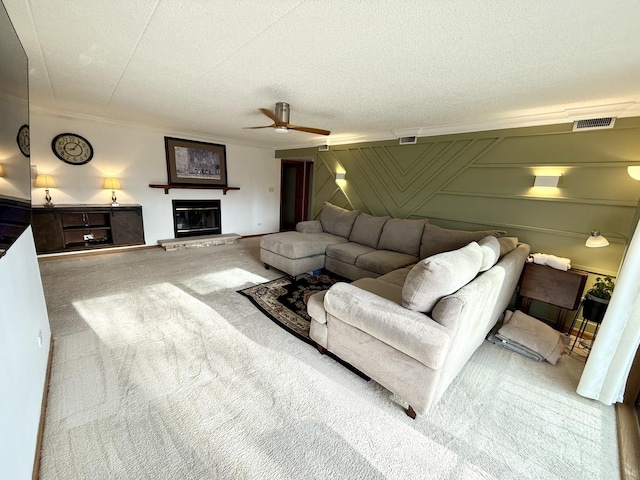 living room with visible vents, carpet, a glass covered fireplace, a textured ceiling, and a ceiling fan