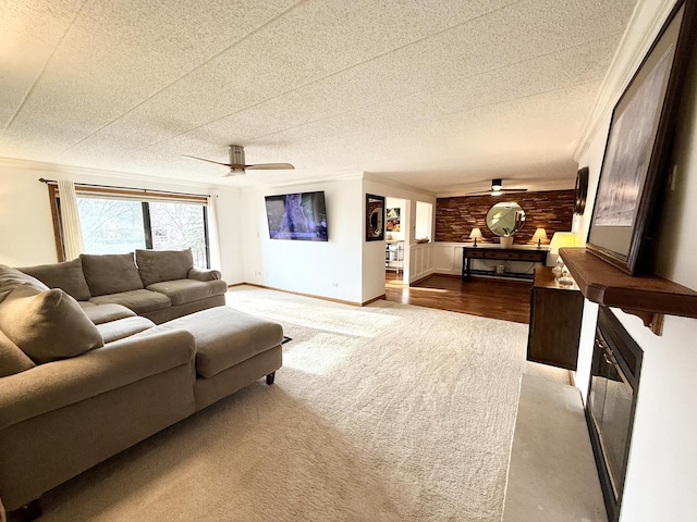 carpeted living room with a textured ceiling, baseboards, crown molding, and a ceiling fan