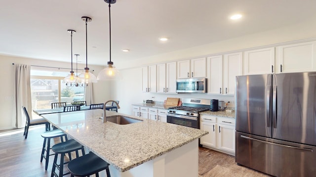 kitchen with a sink, a breakfast bar area, appliances with stainless steel finishes, white cabinetry, and a kitchen island with sink