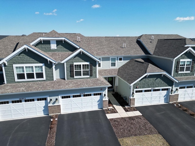 view of front of home with brick siding, roof with shingles, and driveway