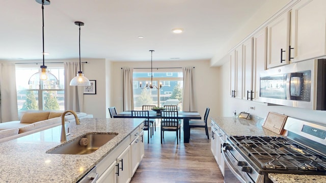 kitchen with wood finished floors, a sink, stainless steel appliances, white cabinets, and a chandelier