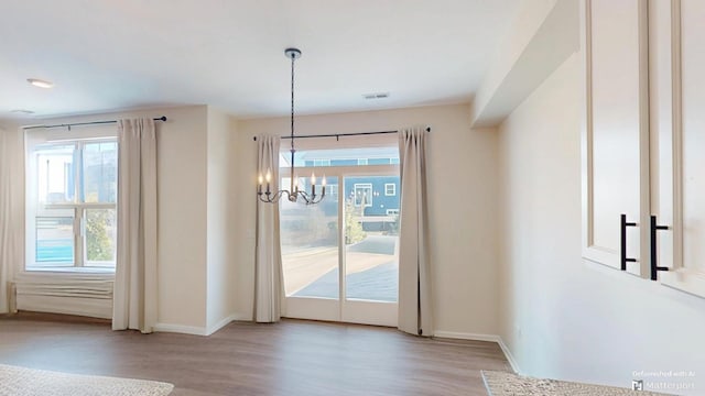 unfurnished dining area featuring an inviting chandelier, wood finished floors, visible vents, and baseboards