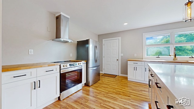 kitchen featuring light wood-style flooring, a sink, stainless steel appliances, white cabinets, and wall chimney range hood