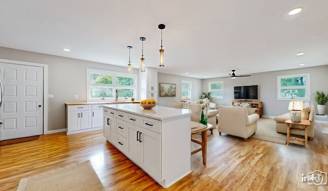 kitchen featuring a center island, ceiling fan, light countertops, light wood-style flooring, and white cabinetry