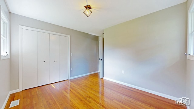 unfurnished bedroom featuring a closet, baseboards, visible vents, and light wood finished floors