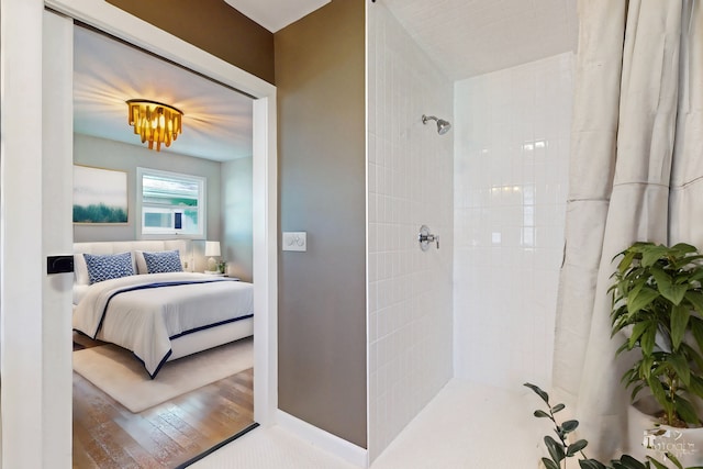 ensuite bathroom featuring wood finished floors, baseboards, a tile shower, and connected bathroom