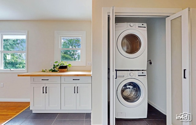 clothes washing area with laundry area, dark tile patterned floors, baseboards, and stacked washer and clothes dryer