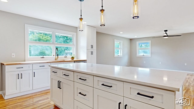 kitchen with ceiling fan, hanging light fixtures, a sink, white cabinetry, and light wood-type flooring