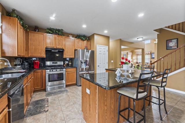 kitchen with a sink, a center island, appliances with stainless steel finishes, a breakfast bar area, and exhaust hood